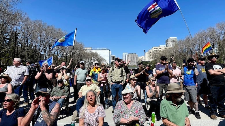 People with Alberta flags gather on the steps of the Alberta legislature.