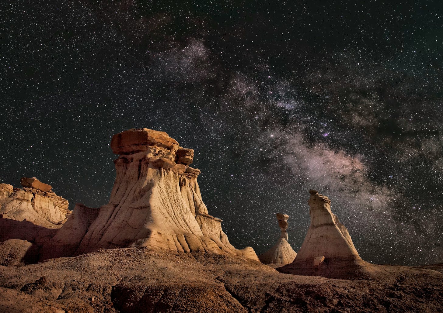 wind sculpted columns on a rough desert against cliffs under a starry sky