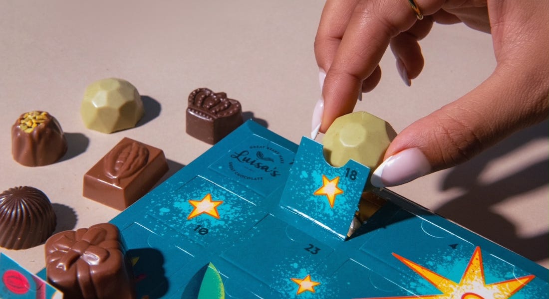 A blue advent calendar with chocolates around it being picked up by a hand with pink nails A blue advent calendar with chocolates around it being picked up by a hand with pink nails