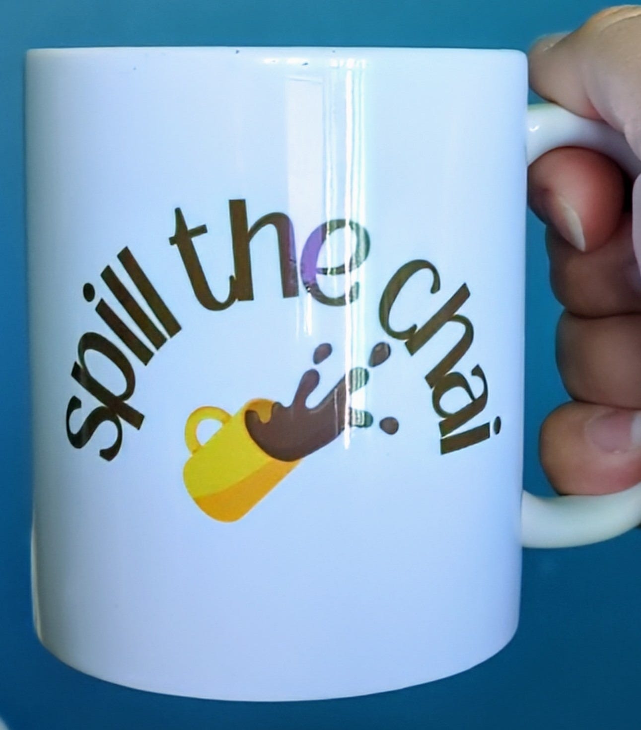 Coffee mug that reads "Spill the chai" with a drawing of a yellow mug being knocked over and splashing brown liquid out of it Coffee mug that reads "Spill the chai" with a drawing of a yellow mug being knocked over and splashing brown liquid out of it