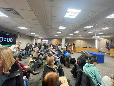 Photos of a packed meeting rooom filled with Carver County citizens testifying in opposition to renting jail cells to ICE