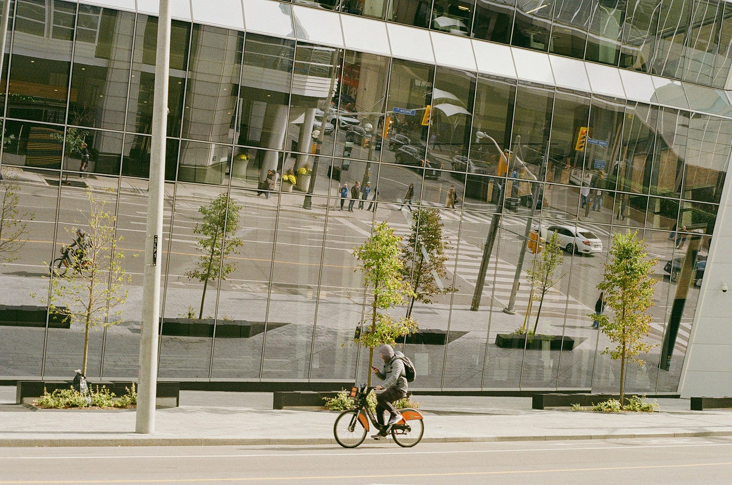 Cyclist passes a glass office building reflecting a modern city intersection.