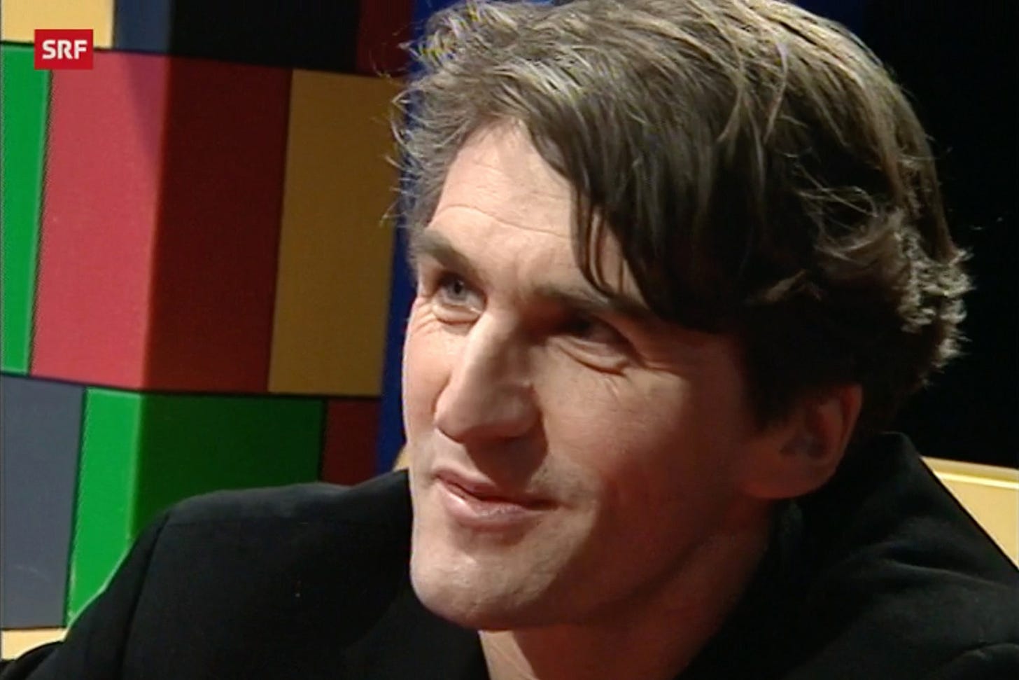 Albert Kuhn während eines Interviews im Fernsehstudio, im Hintergrund bunte Bausteine.