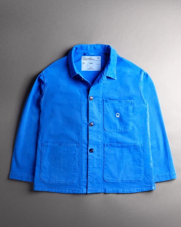 A bright blue chore coat with three buttons on the front and two lower pockets as well as one breast pocket. The tag, with the size large and a small American flag, is visible at the collar. 