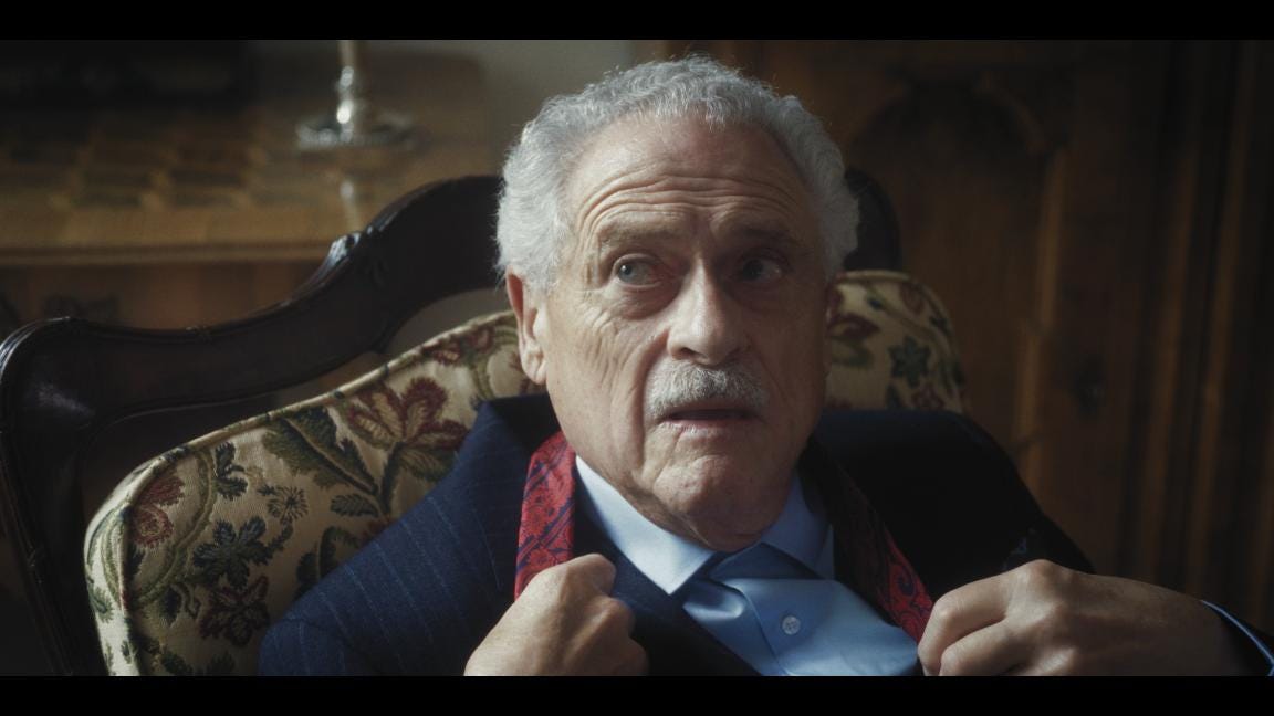 A grey-haired man in a suit changing his tie