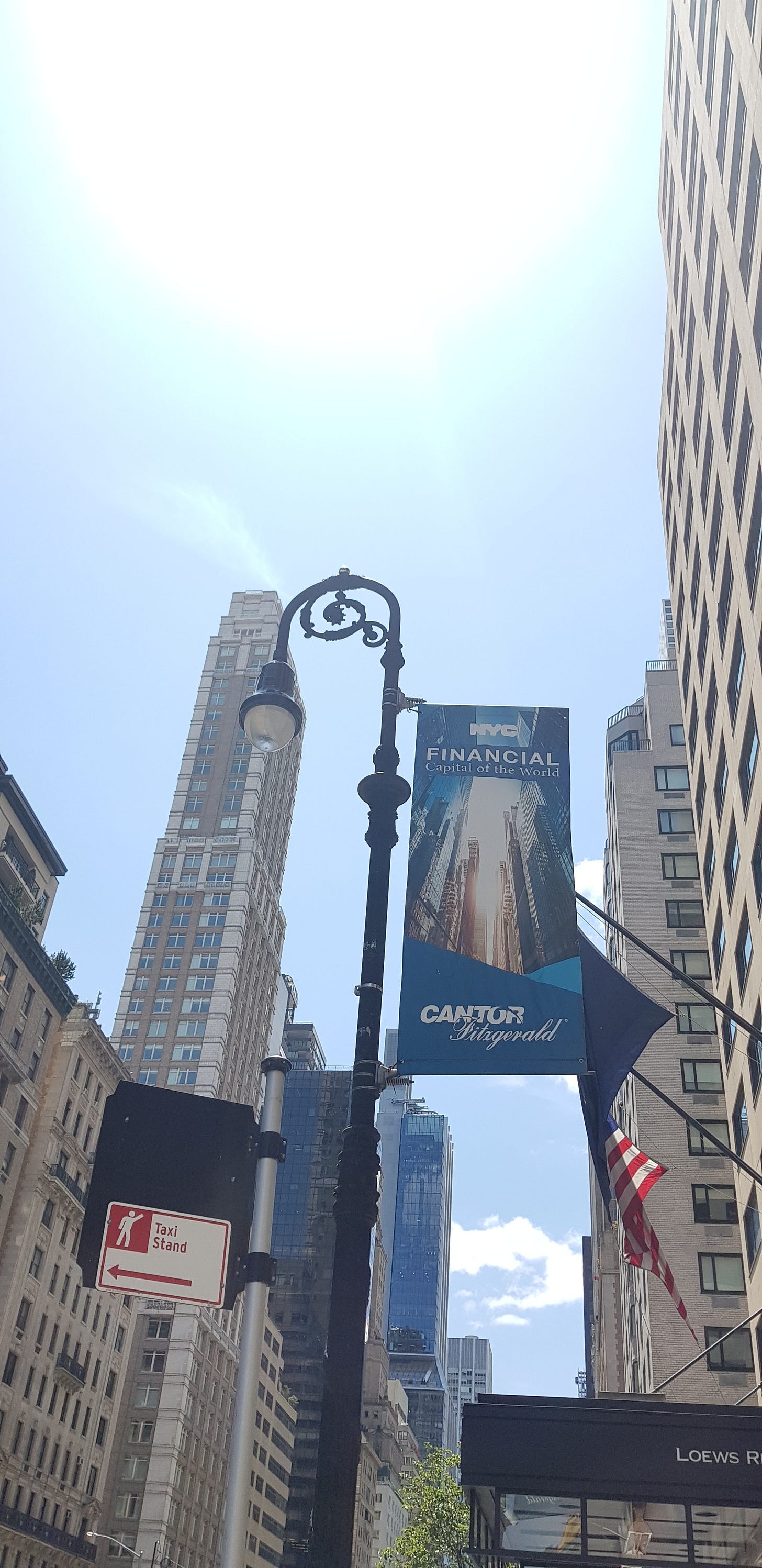 Looking up at a cast-iron street lamp and a banner reading "Financial Capital of the World," with an American flag and towers. Looking up at a cast-iron street lamp and a banner reading "Financial Capital of the World," with an American flag and towers.