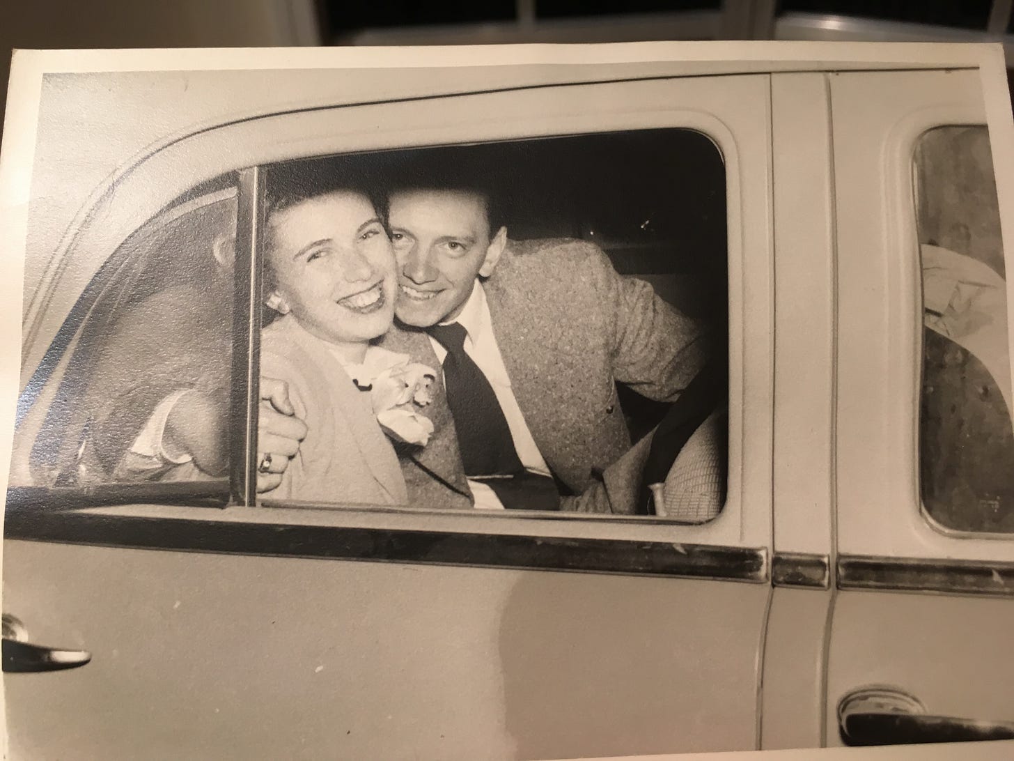 Suz's mom and dad ready to escape to their honeymoon after their wedding. They are impossibly young and smiling very broadly as they sit in the backseat of a car, looking at us out the open window.