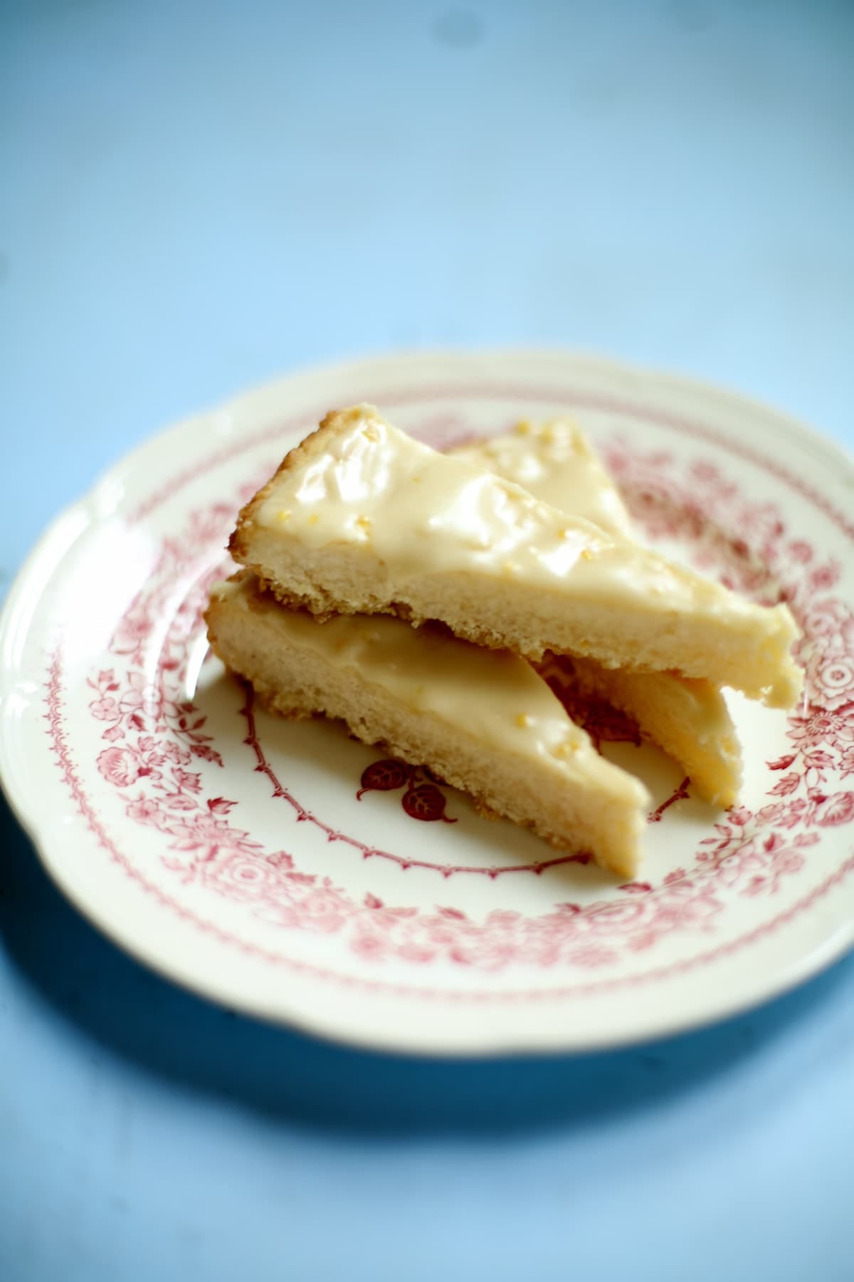 three slices of lemon shortbread cookies on a whte and red plate set on a blue table