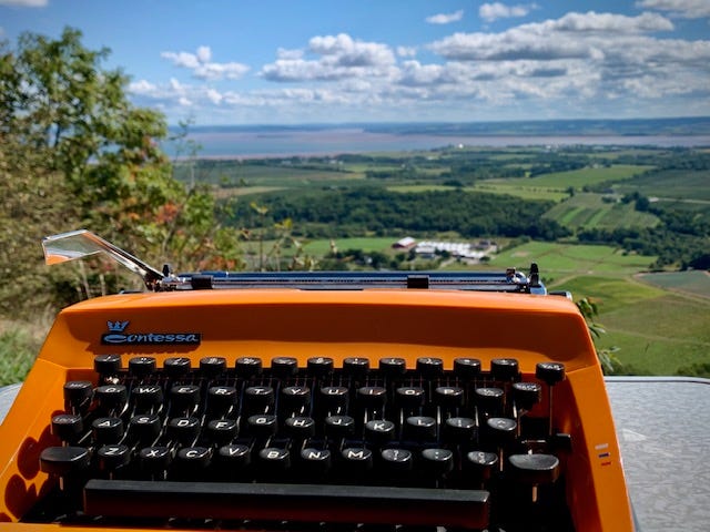 Photo one is a woman in a straw hat sitting with a typewriter overlooking a verdant valley below. Photo two is a bright orange typewriter sitting on a table with a valley in the distance