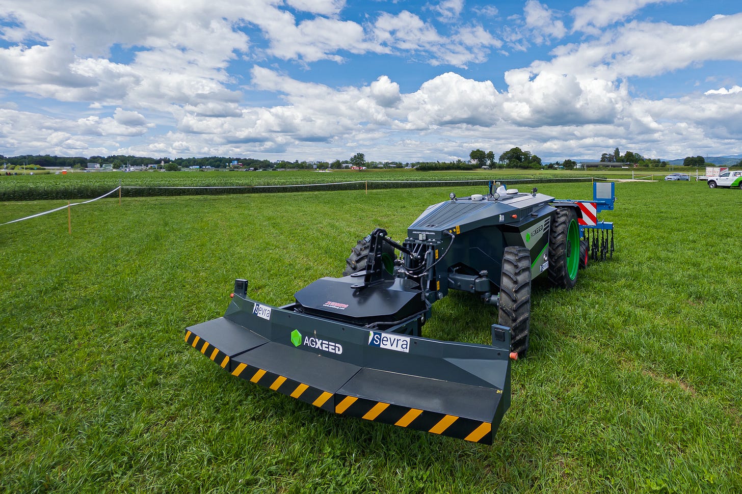 Das Bild zeigt die technische Ausrüstung des autonomen Feldroboters AgBot von AgXeed aus nächster Nähe. Auf dem Dach sind Scheinwerfer, Antennen- oder GNSS-Module und ein hoch montierter 3D-LiDAR-Sensor zu sehen, der der Umgebungserfassung dient. Die glänzende Metalloberfläche spiegelt Licht und Wolken; dahinter öffnet sich eine weite Agrarlandschaft.