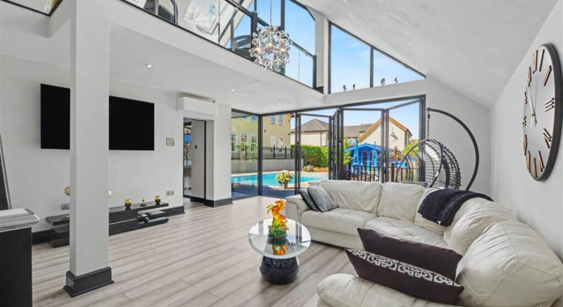 A living room with grey walls, black framed windows, a white sofa, and a pool outside A living room with grey walls, black framed windows, a white sofa, and a pool outside