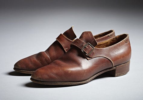 1) Classic black-and-white portrait of Gluck in a loose white shirt/smock, looking down and to the side. Their expression is thoughtful, with shadows adding depth. They have short dark hair, and they are holding a cigarette in their right hand. There is a dark shirt sticking out from under the larger shirt, with both collars sticking up. 2) A white mannequin displays a vintage, cream-colored linen shirt/smock with a black collar and buttoned cuffs, evoking a classic, timeless style. It's positioned in the same style Gluck was wearing it in the previous photo, including the collars sticking up. The mannequin head is also looking to the side, like Gluck was. 3) A pair of vintage brown leather shoes with buckles and low heels on a neutral background, conveying a sense of timeless style and craftsmanship. 4) Five vintage dresses/gowns hang on a black clothing rack with a small jacket. Patterns include floral, paisley, and abstract designs, evoking a nostalgic and elegant feel. 5) A white mannequin displays an elegant black evening gown with a lace overlay. The dress features long sleeves and a floor-length skirt, conveying sophistication.