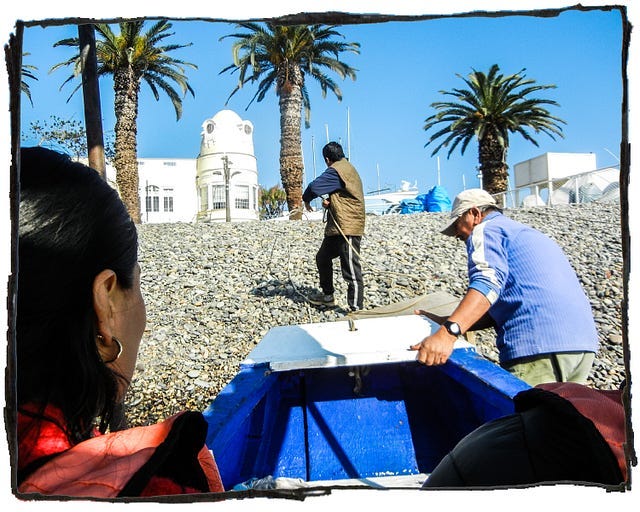 Image of two men pulling a boat onto shore while a woman looks on. There are palm trees in the background.