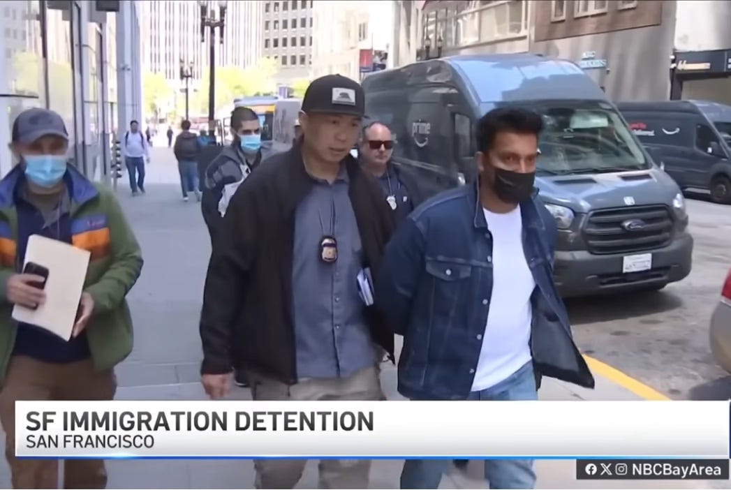 at least four men in plain clothes (with badges on lanyards visible) escort a handcuffed man on a sidewalk in San Francisco