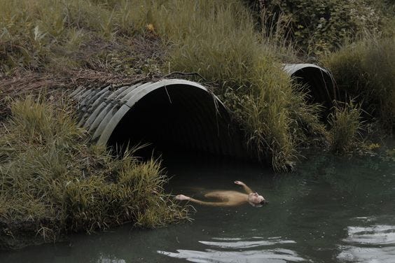 This may contain: there is a man swimming in the water next to two large pipes that have grass growing out of them