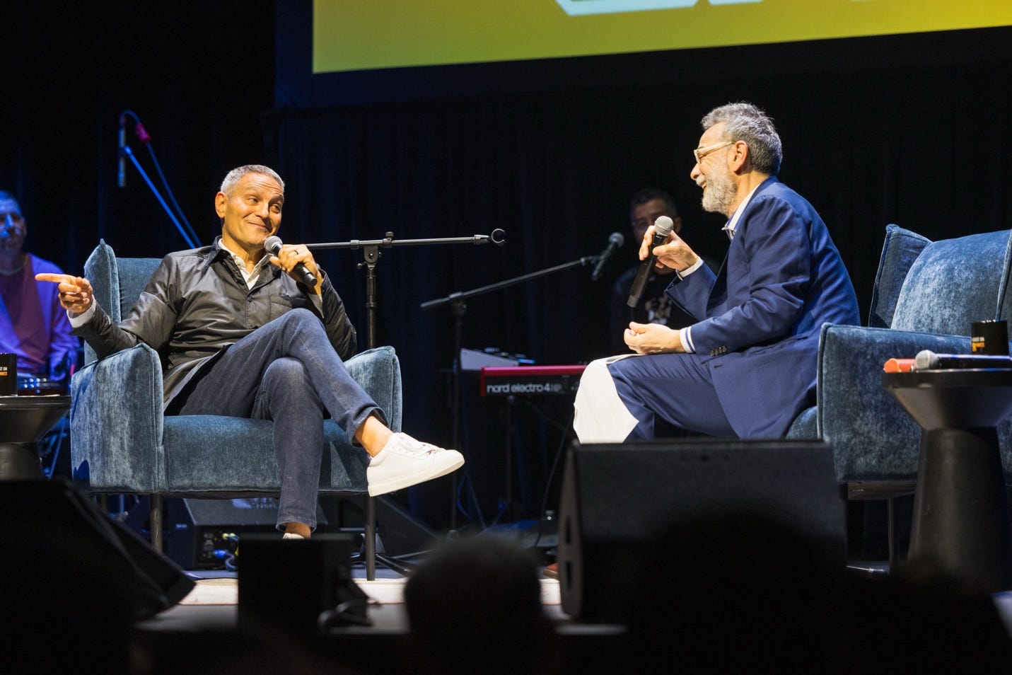 A pair of men sitting on chairs with microphones

Description automatically generated