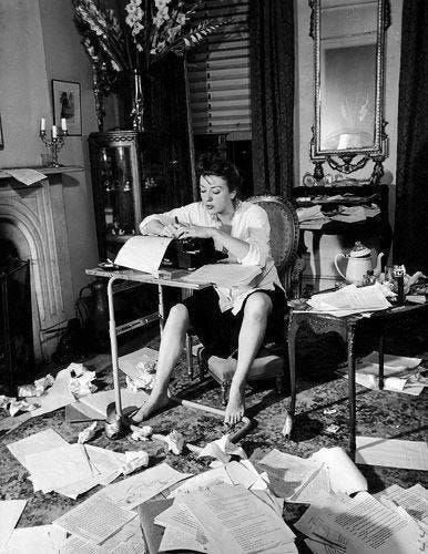 This may contain: a woman sitting at a desk with papers all over the floor in front of her