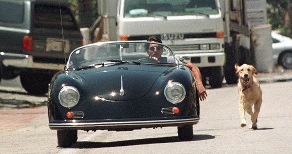 This may contain: a man driving a car down a street next to a dog