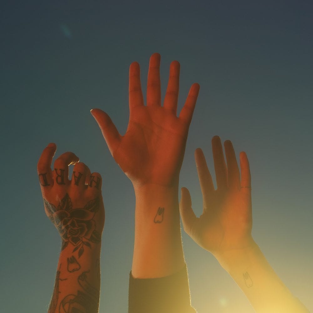 three outstreched hands (one for each band member) rise up on a twilight sky. Light comes from the bottom right corner. Each arm has a matching tatto of a tooth near the wrist.