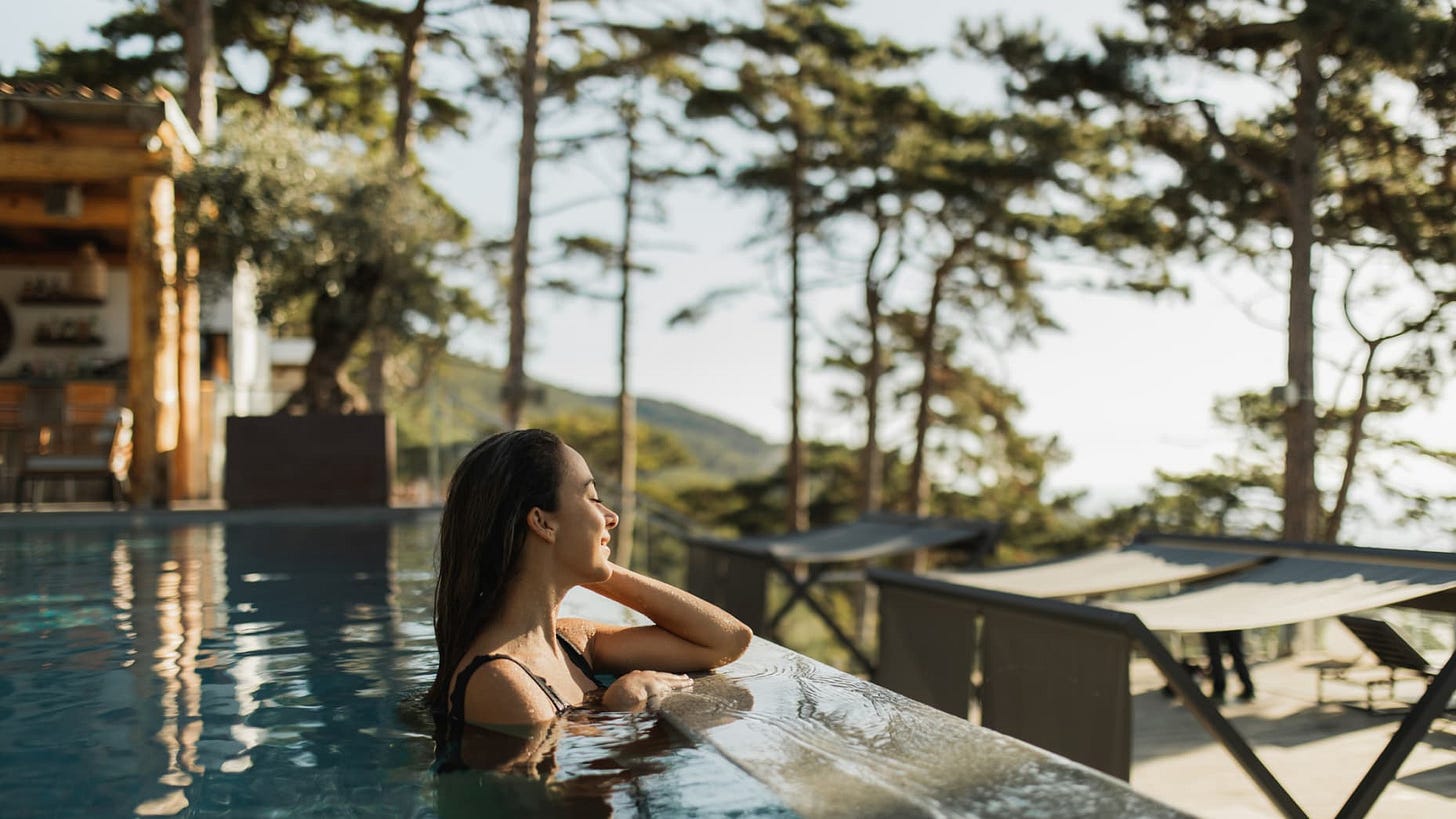 Young cheerful lady enjoying on poolside. Resting in spa hotel in pine forest in summertime. Swimming pool in tourist resort. Joyful woman on vacations, female wellbeing.
