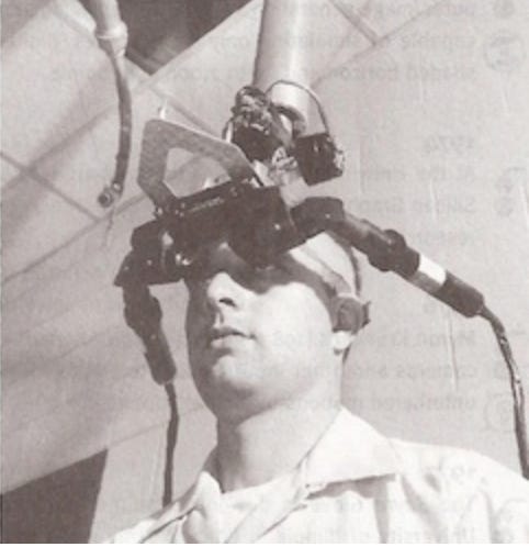A man wears a device on his head, suspended from the ceiling with two large cables coming out from either side of the head-worn apparatus. The picture is black and white. A man wears a device on his head, suspended from the ceiling with two large cables coming out from either side of the head-worn apparatus. The picture is black and white.