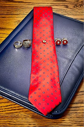 Red tie with polka dots on a blue leather folder, surrounded by rings and cufflinks on a wooden table.