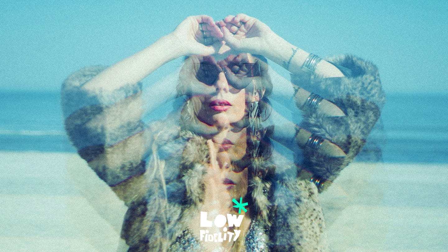 Double-exposure portrait of a woman wearing sunglasses and a fur coat on a beach, her hands raised to her face forming circles around her eyes; layered duplicates of her face and arms create a dreamlike, distorted effect. “Low Fidelity” text appears at the bottom.