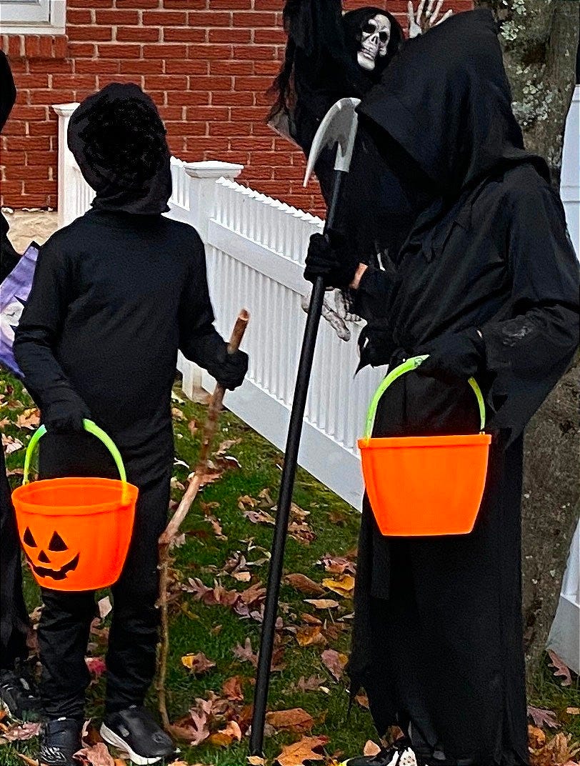 2 Kids in black costumes with faces covered holding pumpkin trick or treat baskets