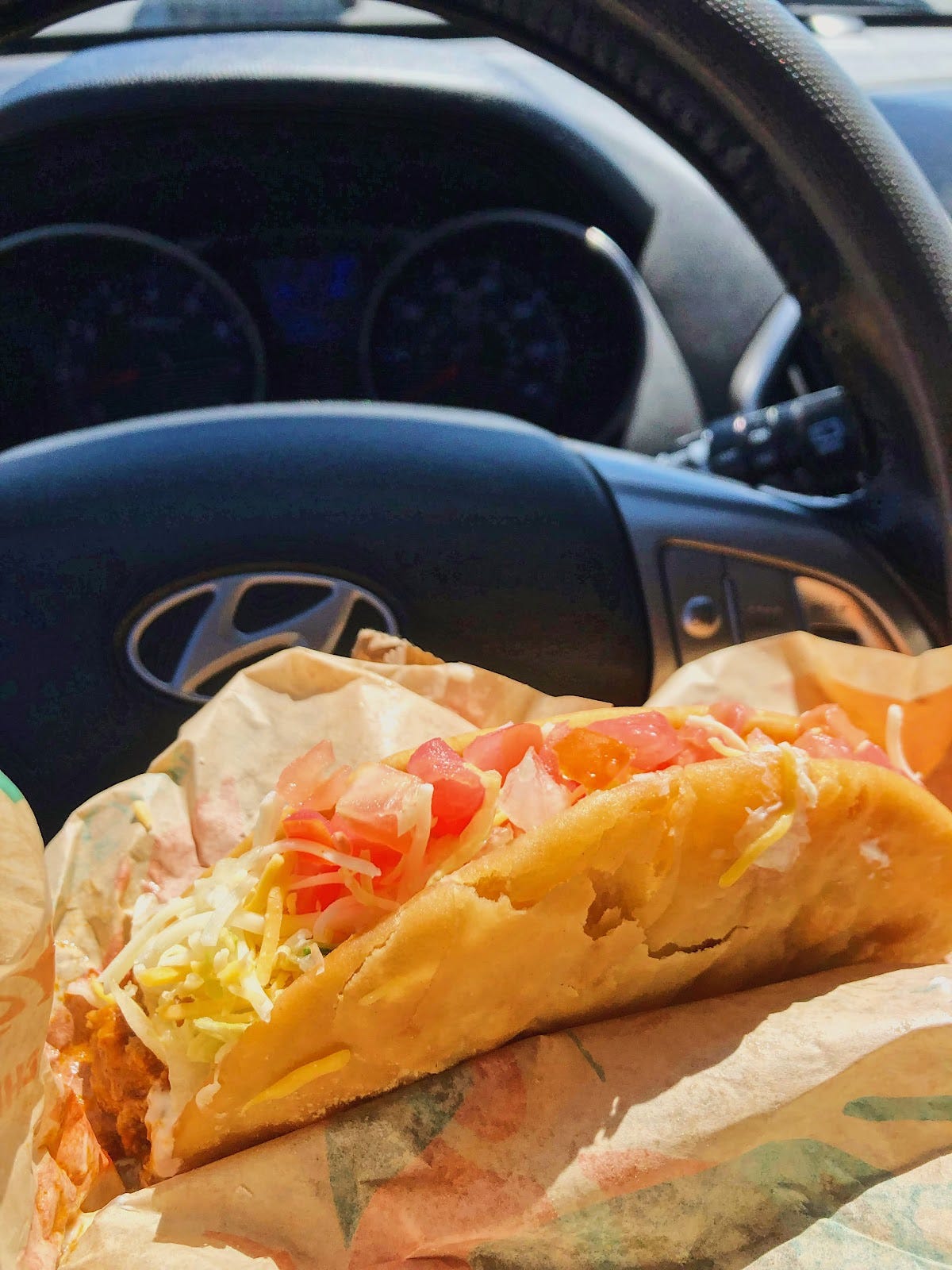 A Taco Bell chapula in the car, with a steering wheel in the background.