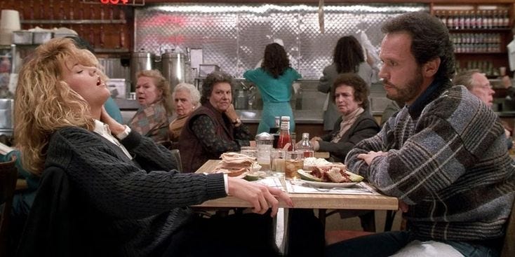 This may contain: a man and woman sitting at a table with food in front of them while people look on