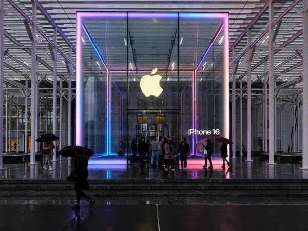 People leave a glass Apple store beneath a metal canopy on a rainy evening.