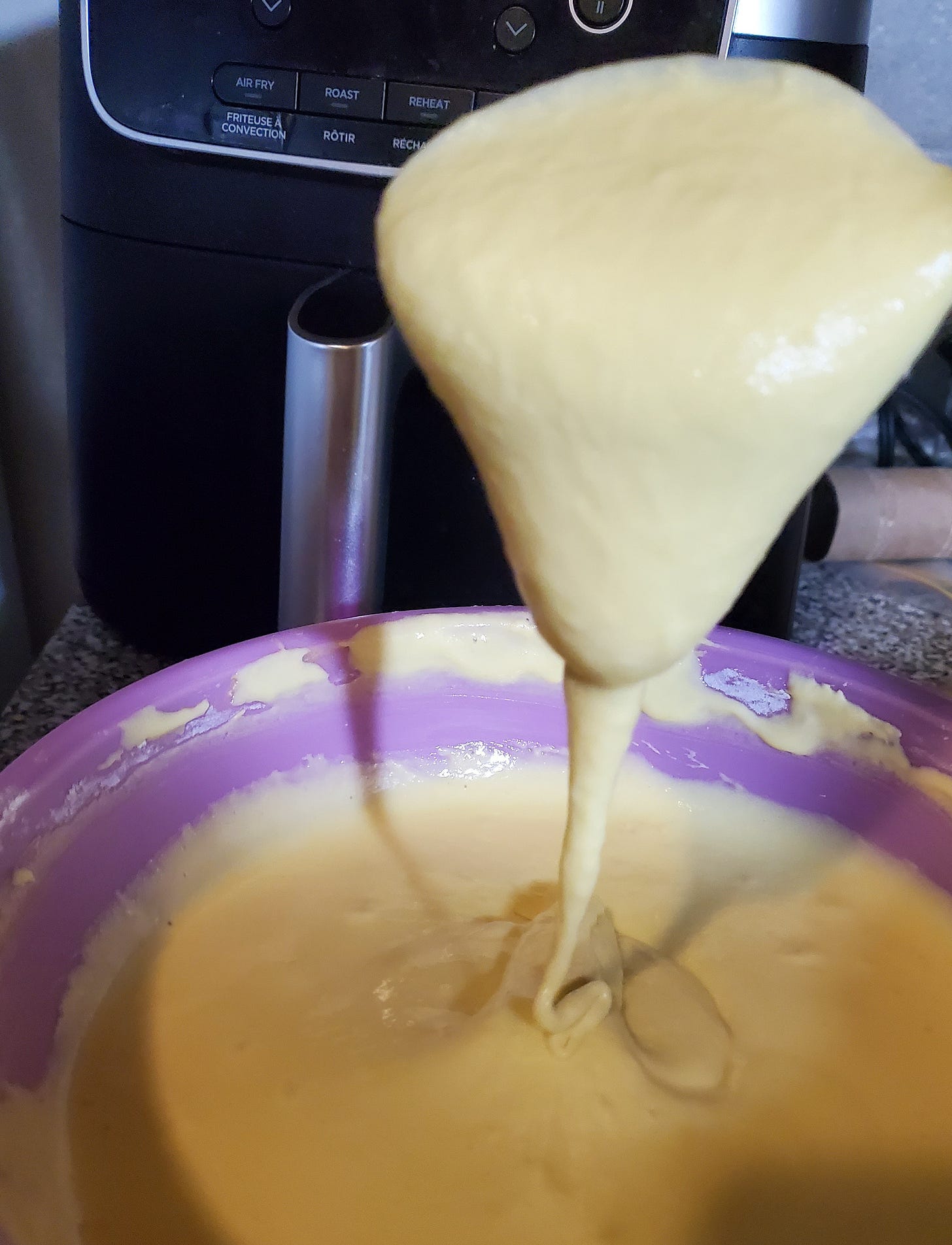A pale yellow mixture flows from a spoon into a pink bowl.