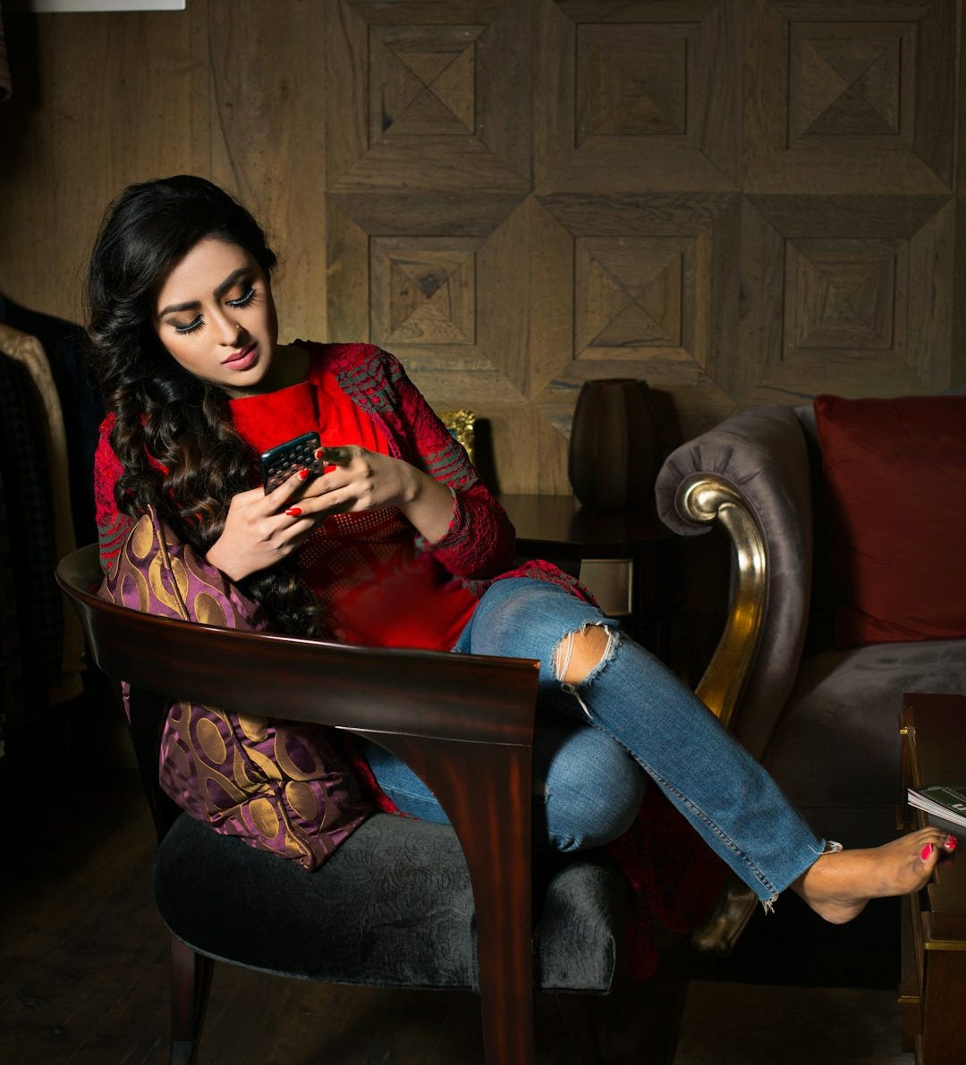 woman in red and white long sleeve shirt sitting on brown wooden armchair woman in red and white long sleeve shirt sitting on brown wooden armchair