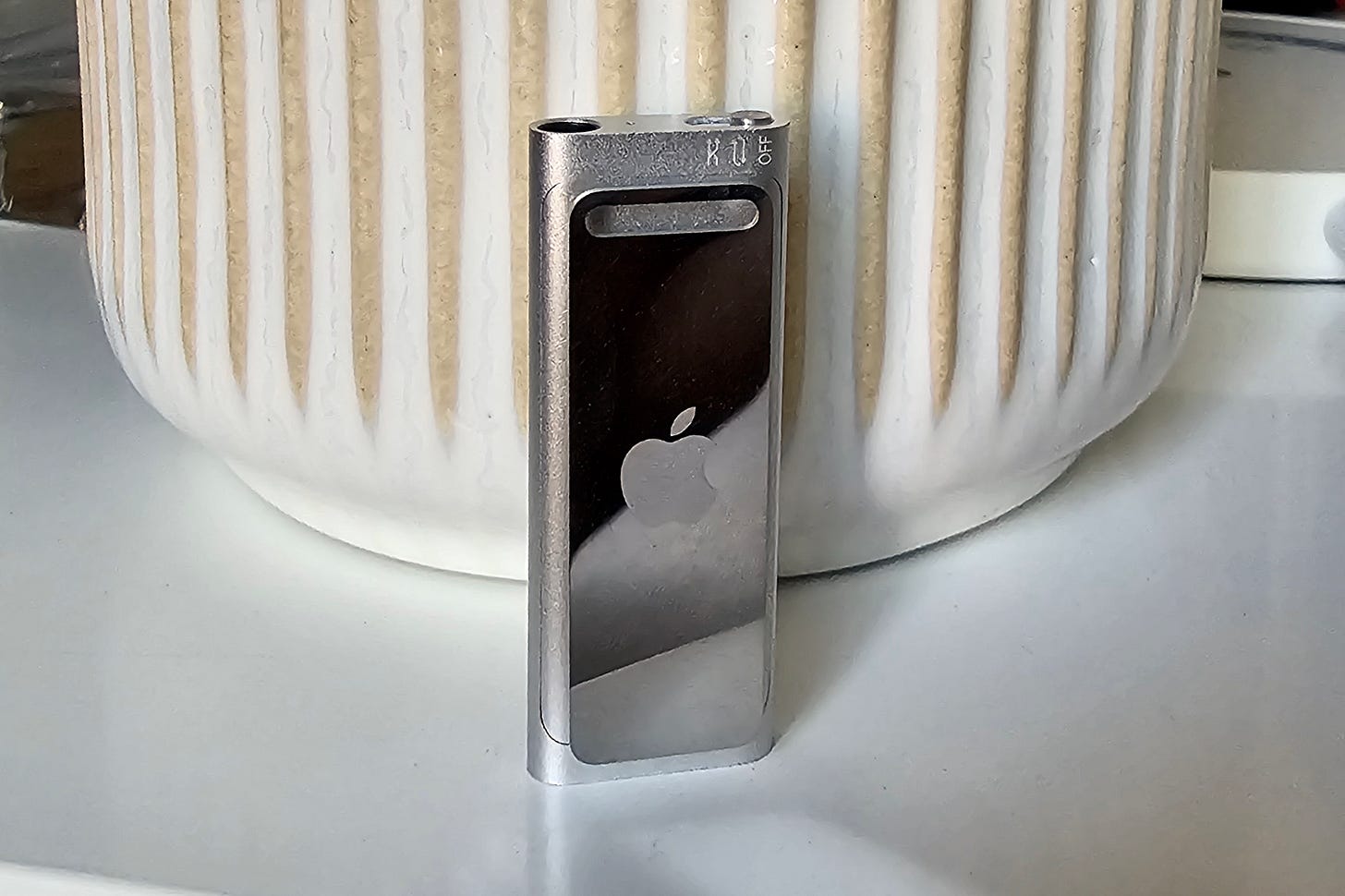 3rd gen Apple iPod Shuffle sitting upright on a desk, no earbuds. 3rd gen Apple iPod Shuffle sitting upright on a desk, no earbuds.