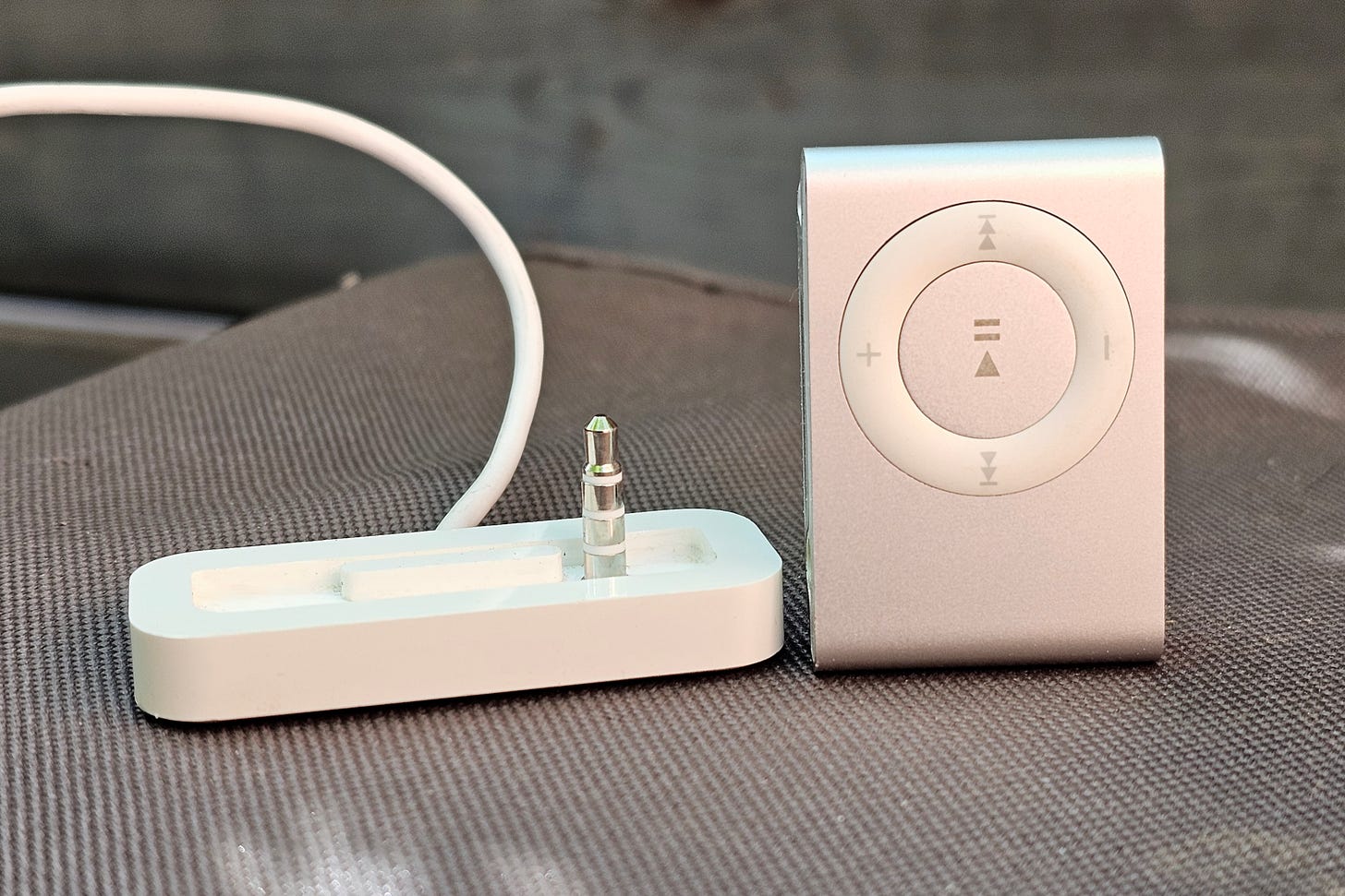 4th-gen Apple iPod Shuffle in silver sitting next to its charging and sync cradle. 4th-gen Apple iPod Shuffle in silver sitting next to its charging and sync cradle.