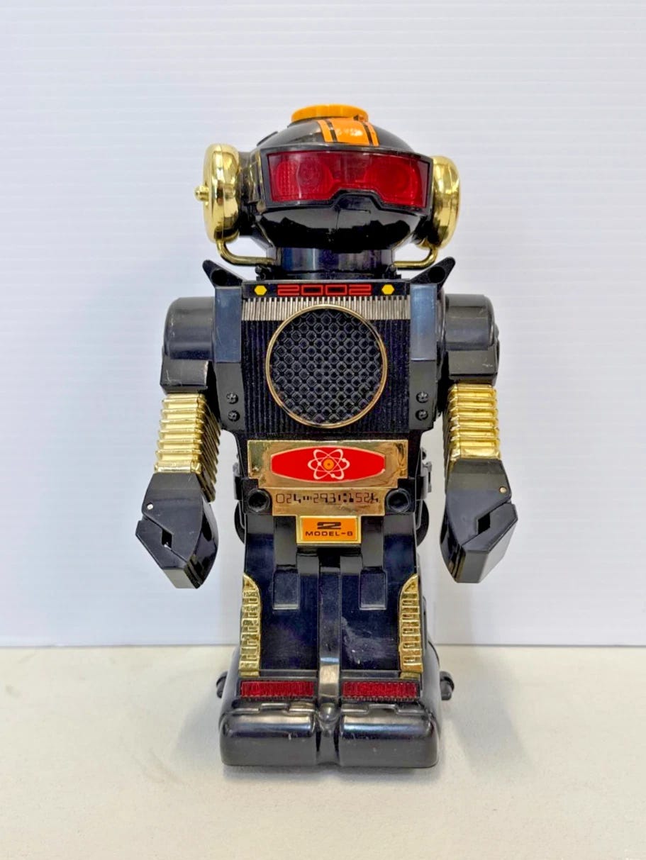 Black 1980 Atomic Robot Tommy with gold chest, red/white arm design, and “Model-B” label on back panel. Black 1980 Atomic Robot Tommy with gold chest, red/white arm design, and “Model-B” label on back panel.