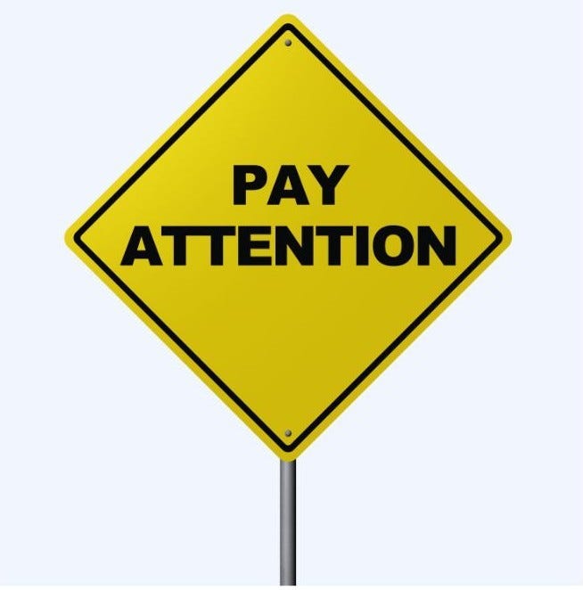 A yellow diamond shaped road sign alerting drivers to "Pay Attention"