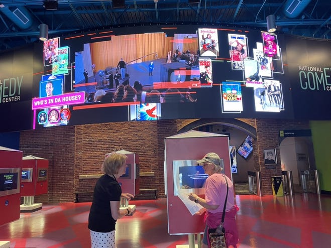 The vibrant interior features a large digital screen displaying various comedy-themed images and videos.