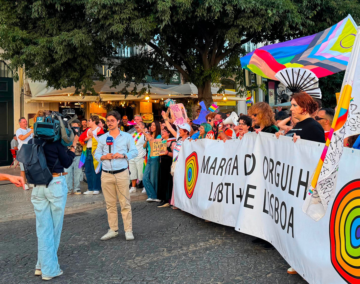 A TV reporter speaks to a camera in front of the Lisbon Pride march banner. A TV reporter speaks to a camera in front of the Lisbon Pride march banner.
