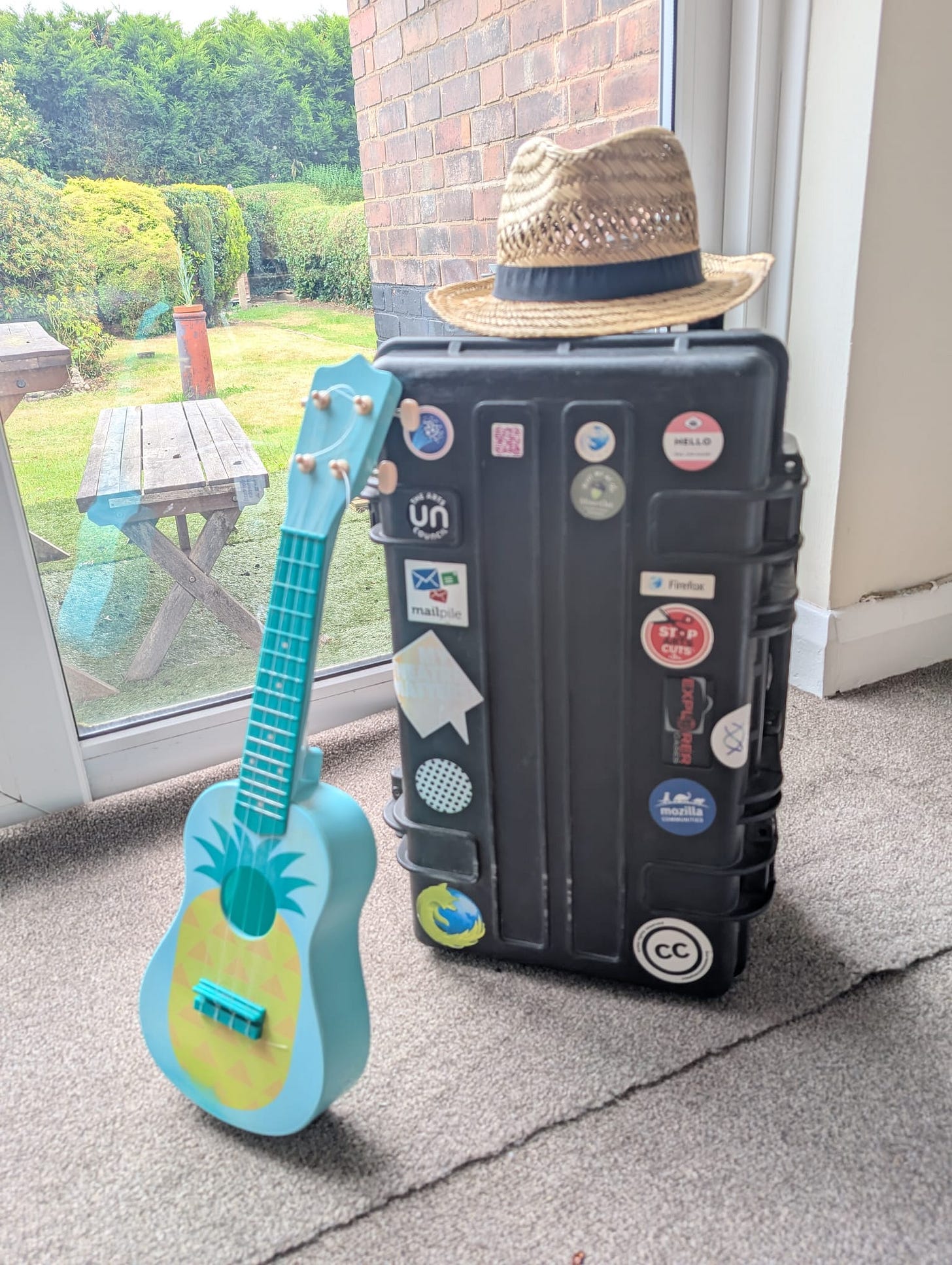 A suitcase adorned with stickers and a hat, prepped for a tech event as I relax on my holiday.