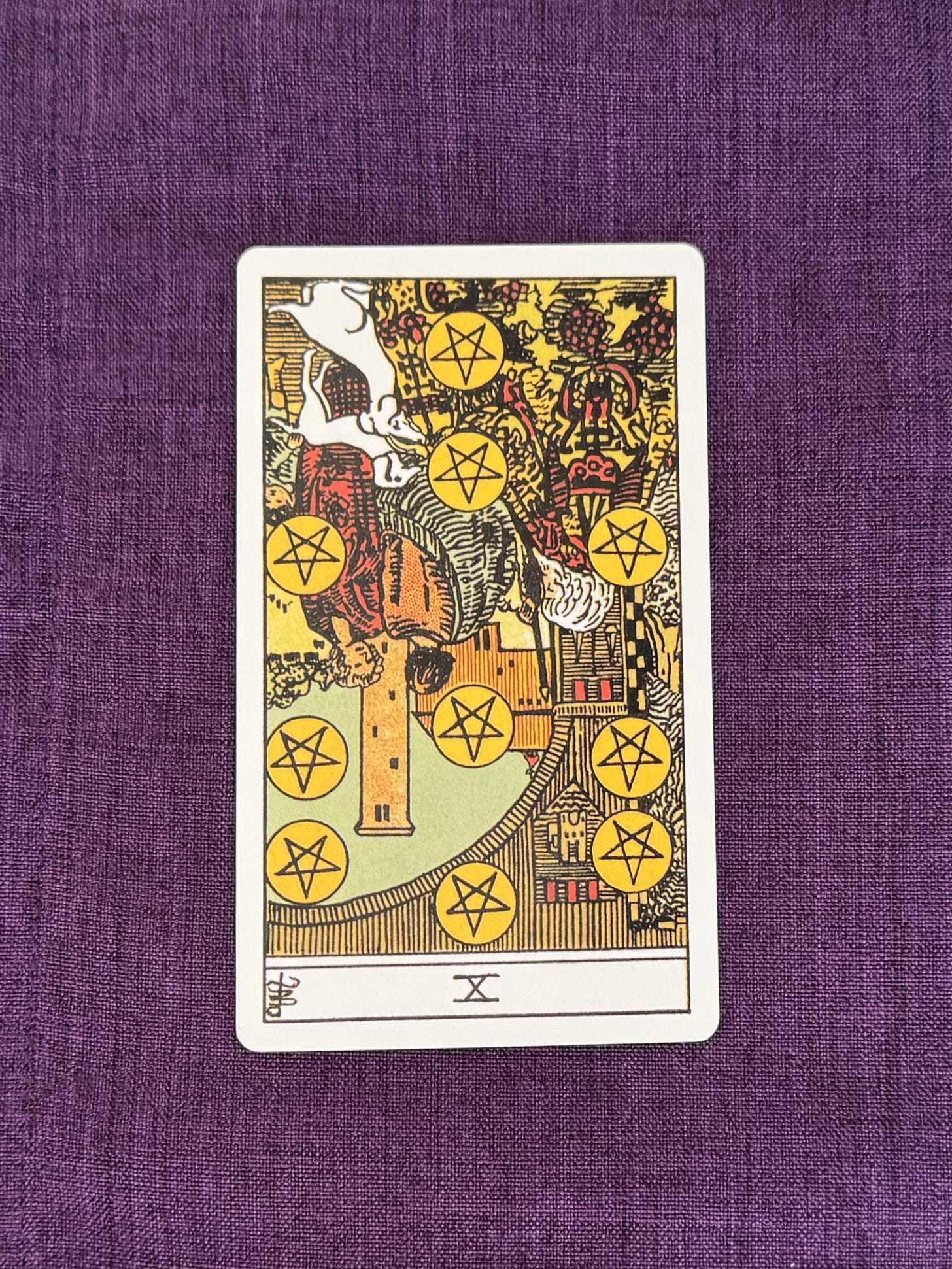 The Ten of Pentacles shows an old, white-haired man wearing an ornately embroidered robe, sitting with two white dogs at his feet. A younger couple stands nearby with a small child. The man and his family are gathered in the courtyard of a large castle. On the archway are emblems and flags. The Ten of Pentacles shows an old, white-haired man wearing an ornately embroidered robe, sitting with two white dogs at his feet. A younger couple stands nearby with a small child. The man and his family are gathered in the courtyard of a large castle. On the archway are emblems and flags.