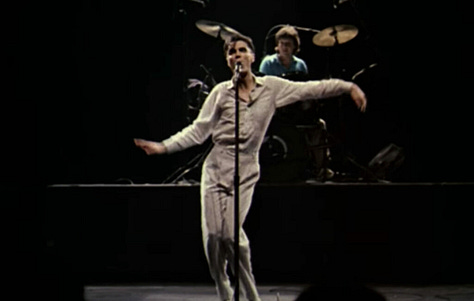 selects from Talking Heads' concert film Stop Making Sense. images of Byrne holding a microphone to camera, raising his arms, dancing in a big suit an with a lamp and full shots of the band.