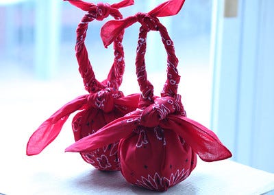 Two round gifts, each wrapped in a red bandana, with the ends twisted and tied into a loop to create a handle.