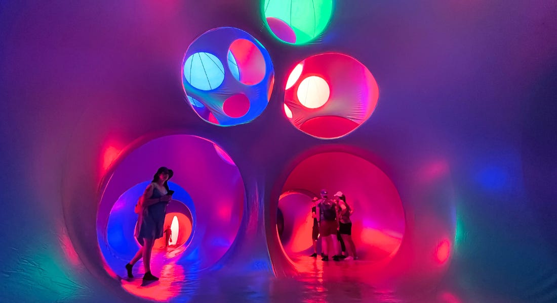 A luminarium with bright lights, pods, and people walking around it