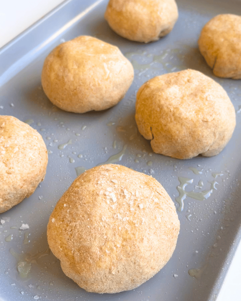 six whole wheat pizza buns on a baking tray, topped with oil and sea salt