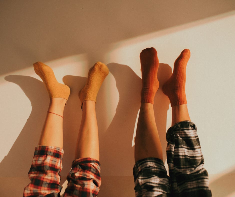 Image of two sets of legs against a wall, with feet in the air. The people are wearing plaid pajama pants and socks.