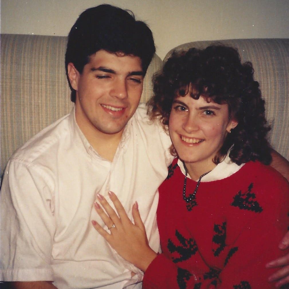 Happy young couple cuddled on the sofa shows off her new engagement ring