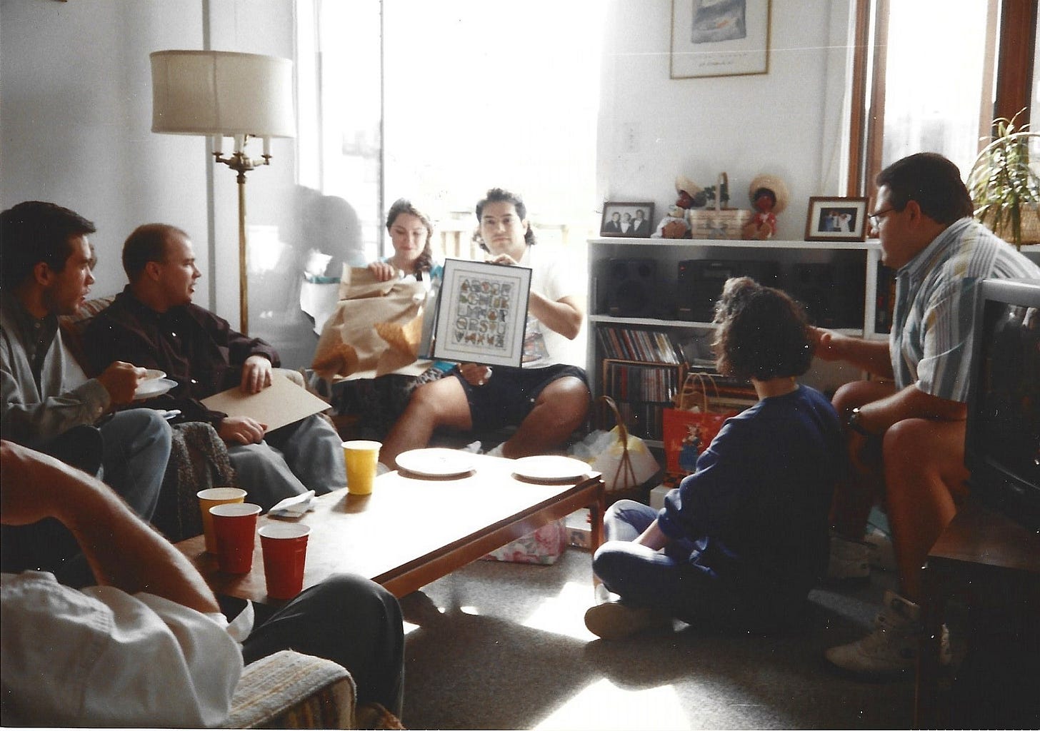 People watching a man hold up a framed cross stich he just opened as a gift