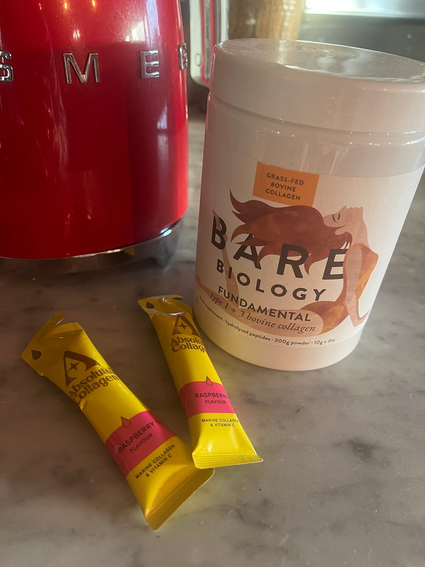 A real-life comparison of Absolute Collagen liquid Marine sachets and Bare Biology Fundamental Bovine collagen powder on a marble counter for The Beauty Ed® guide.