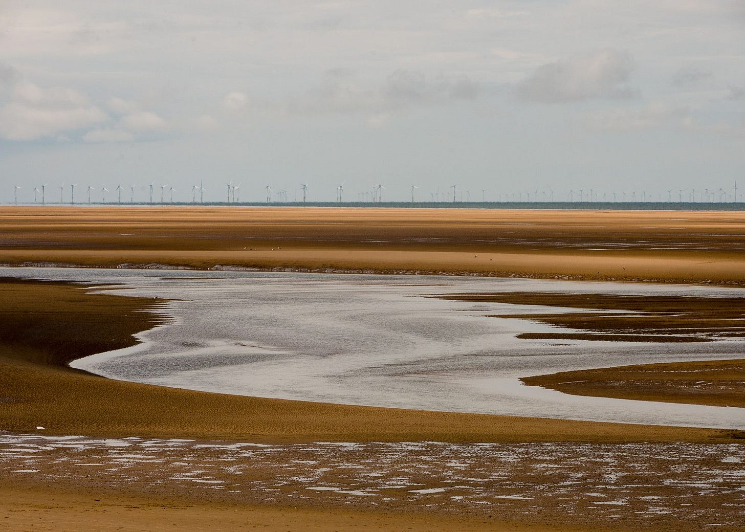 Wind turbines on the horizon with a large river of water filtering through the sand below.